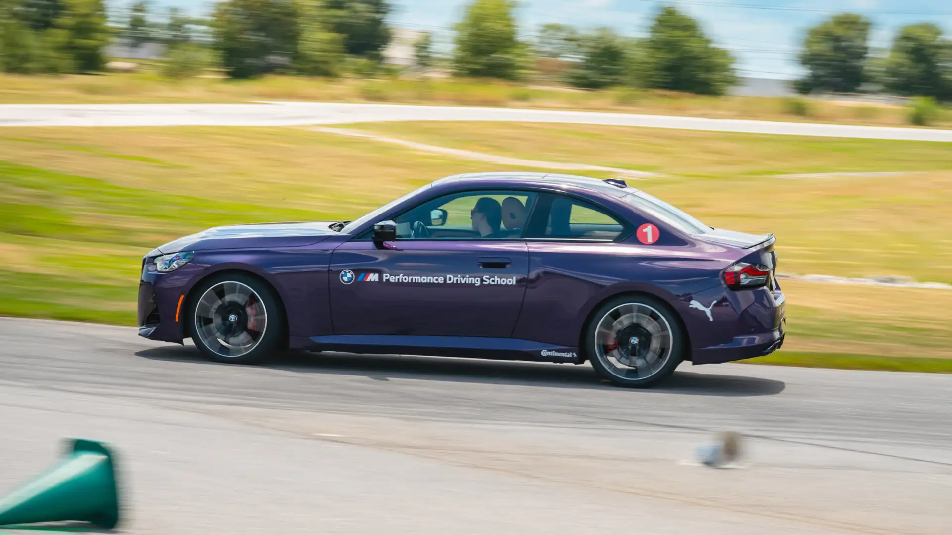 Purple BMW M2 at speed on the circuit past the barriers