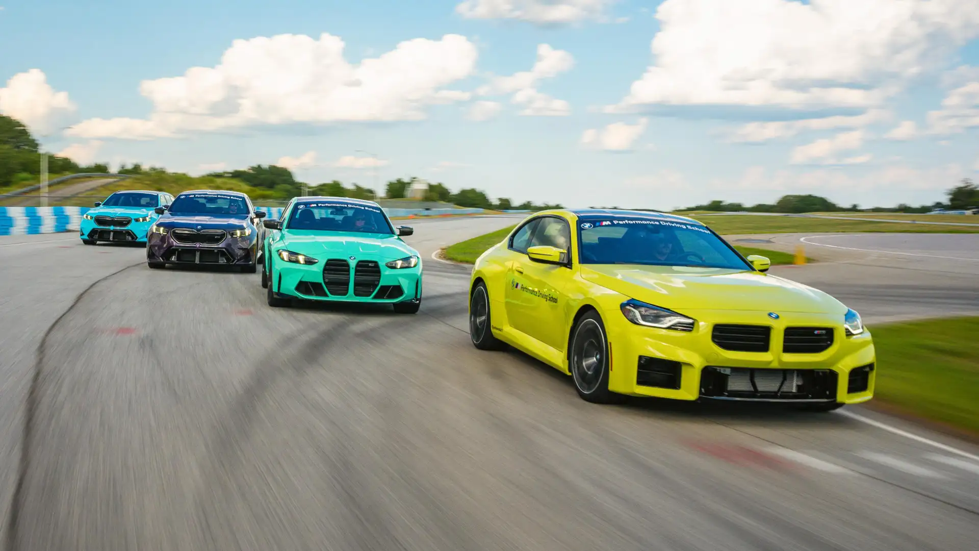 Four BMW M cars running abreast on the South Carolina circuit, led by a yellow M2