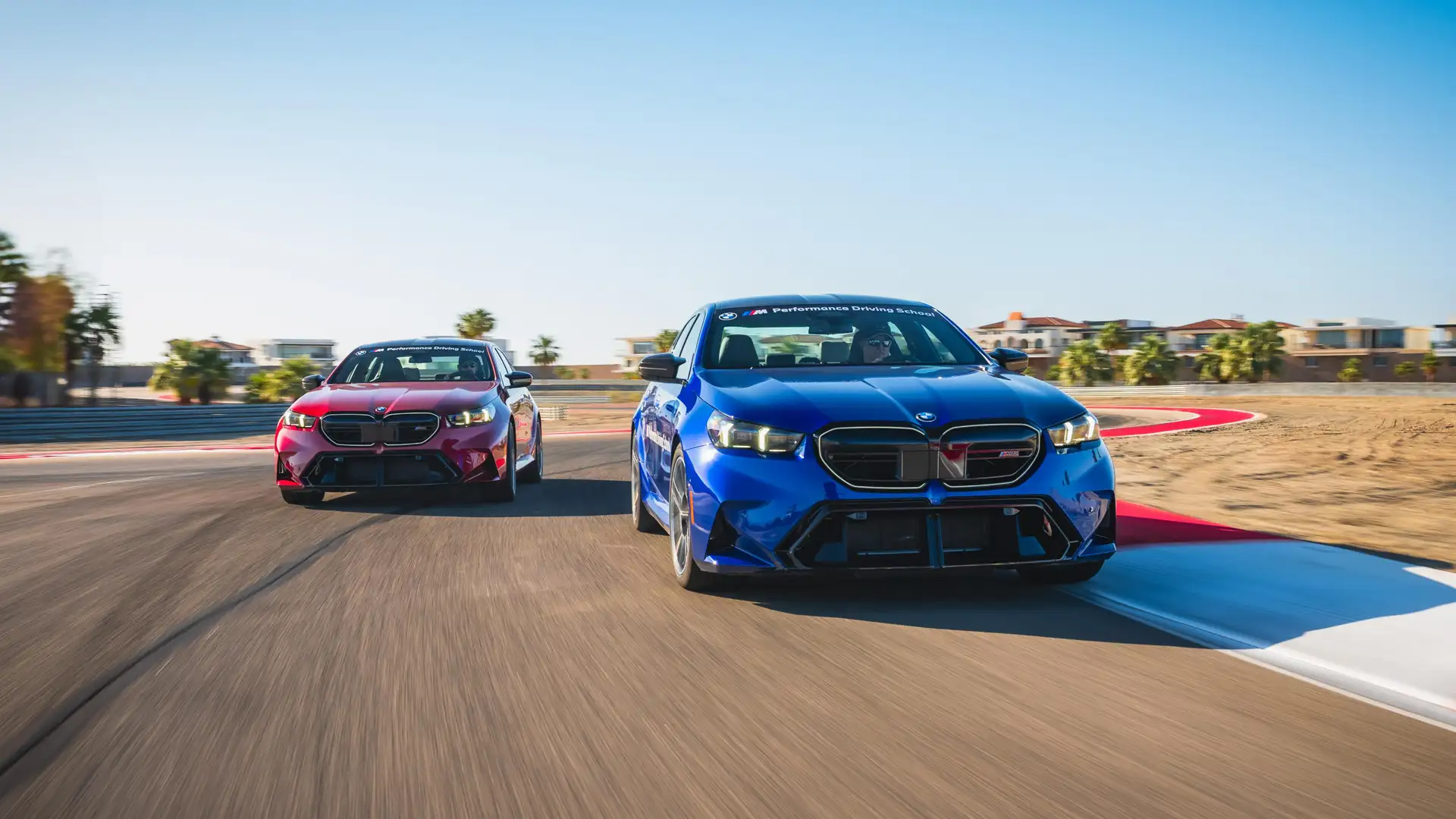 Blue BMW M5 leading a red M5 through a corner on the desert circuit
