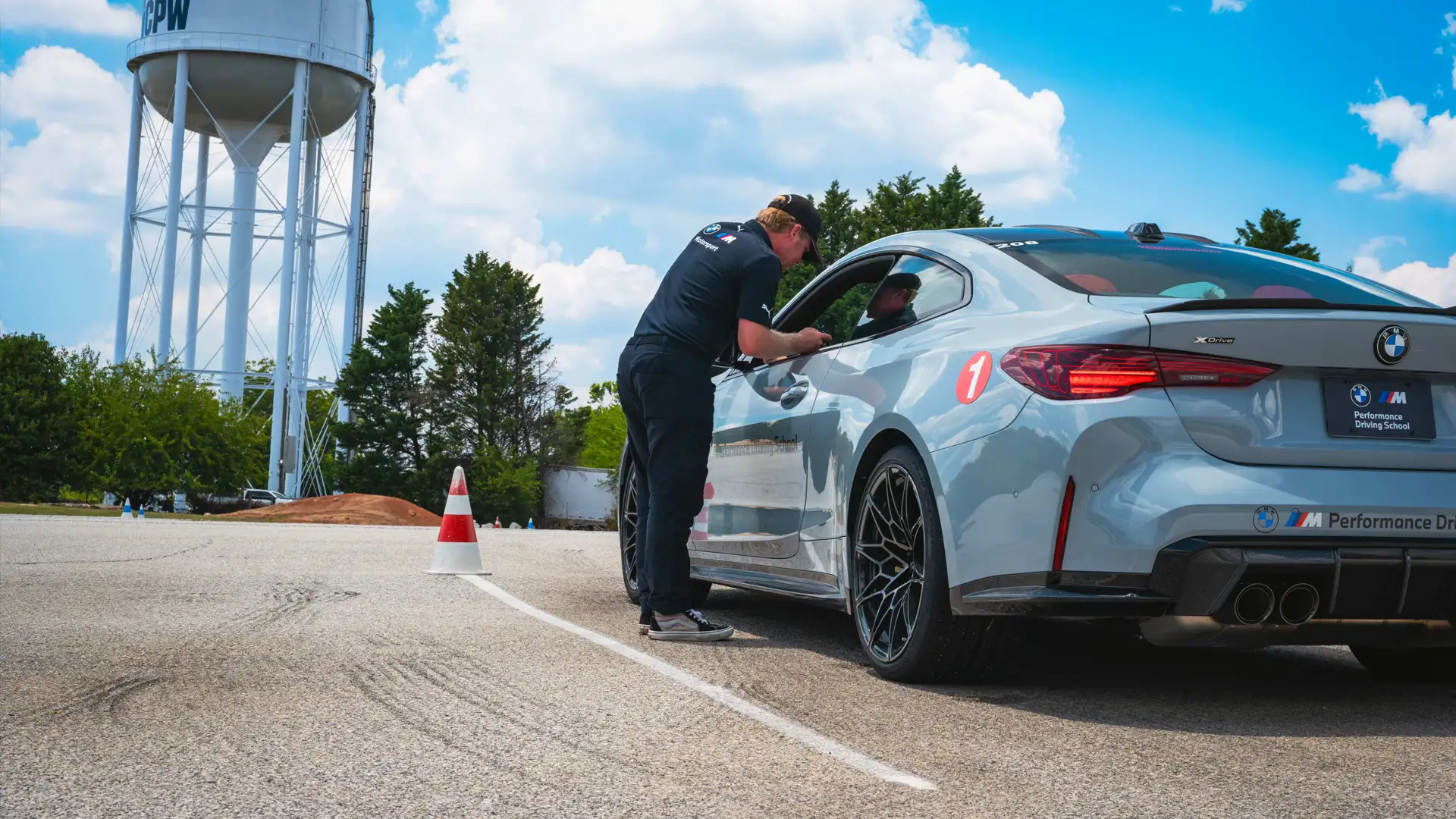 Instructor leaning into the window of a grey BMW M4 to brief the driver