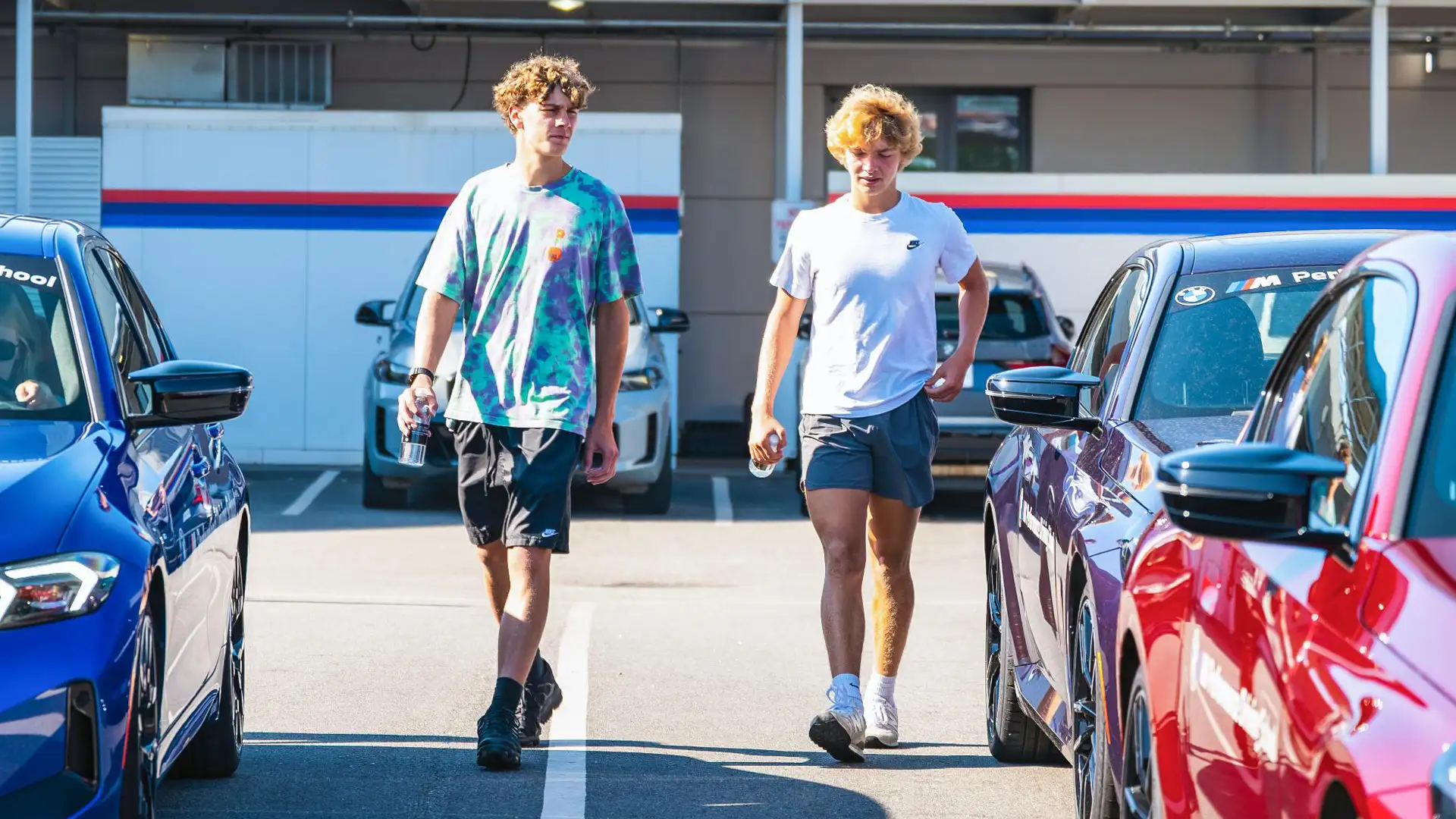 Two teenage students walking between BMW Performance Driving School cars in the paddock