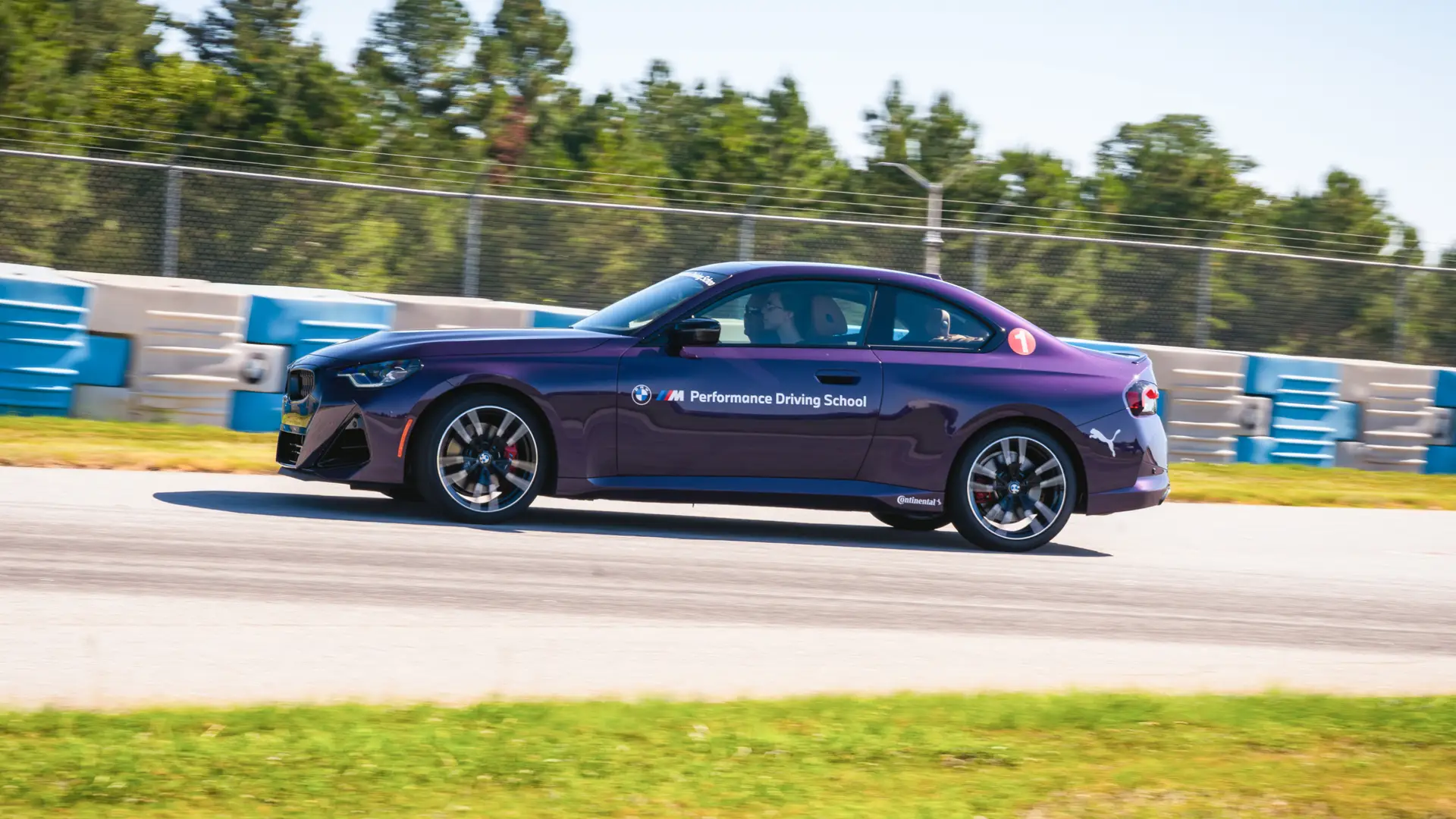 Purple BMW M2 at speed past the blue barriers