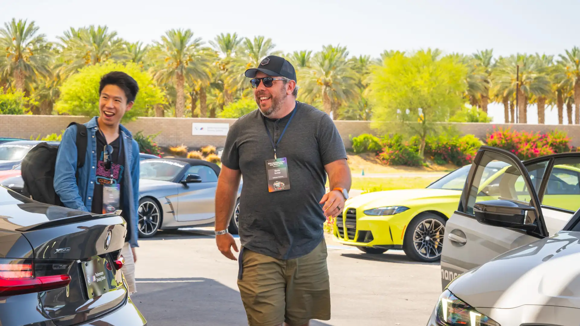 Two participants laughing as they walk through the paddock between BMW M cars