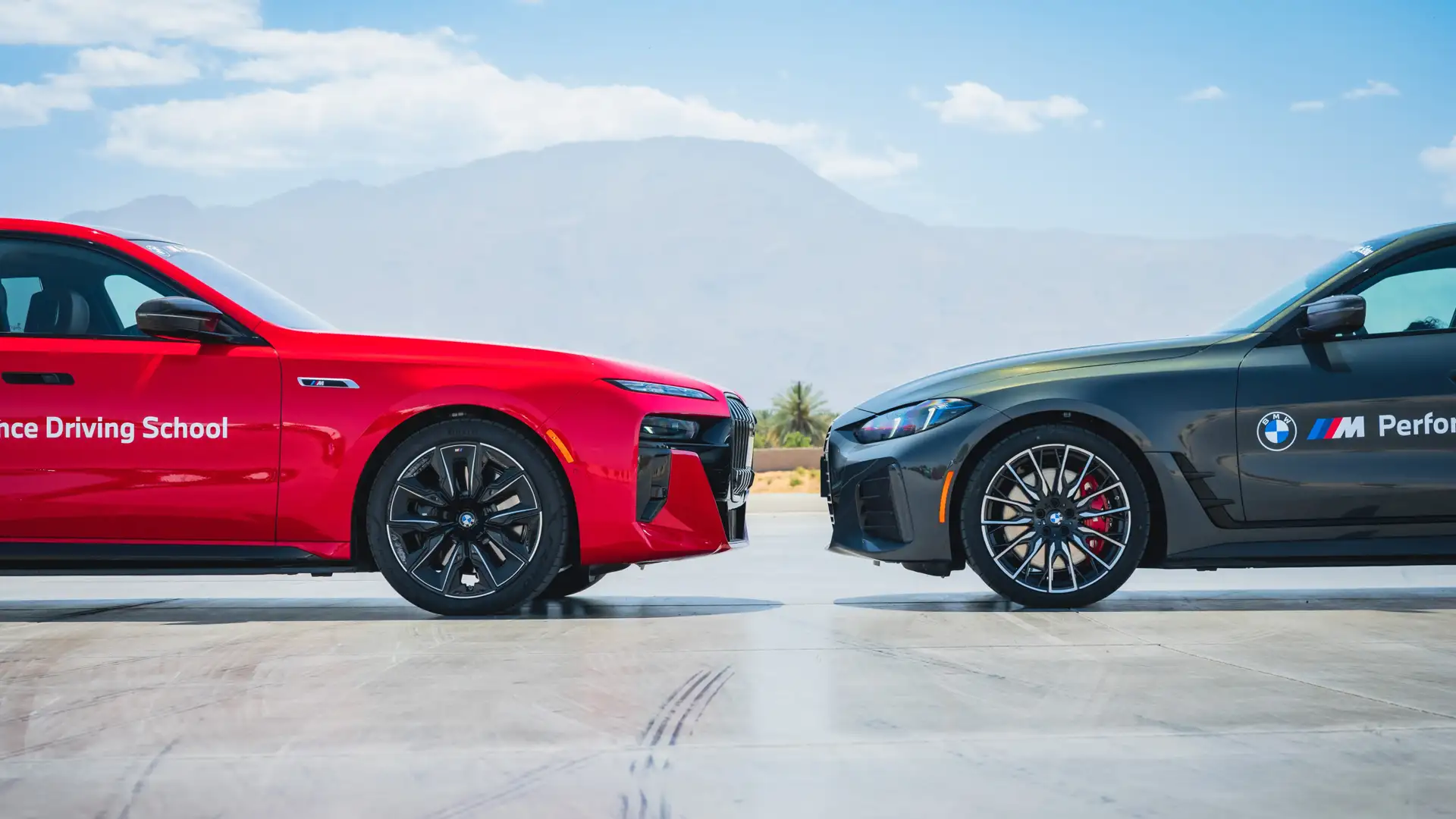 Red BMW i7 and dark BMW i4 parked nose to nose against desert mountains