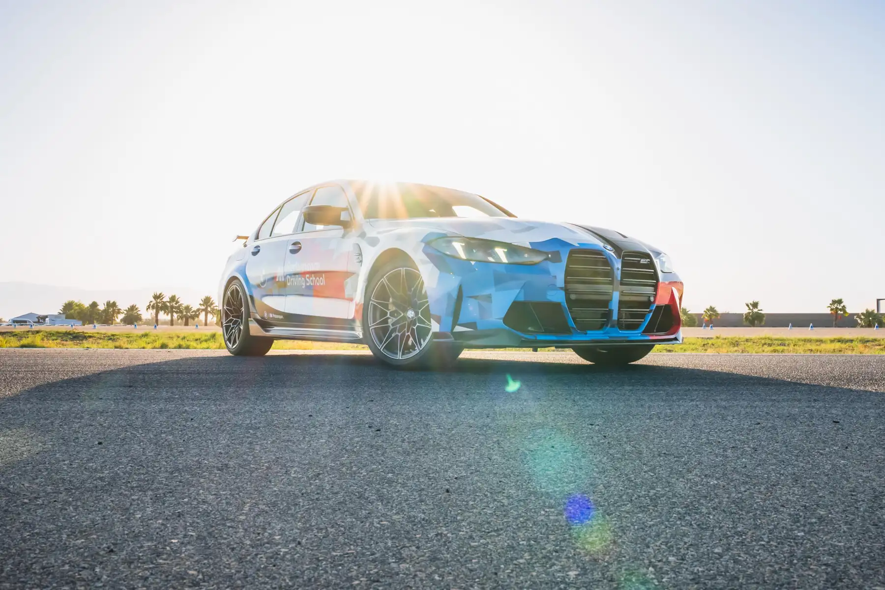 BMW M3 in Motorsport livery parked with the sun behind it