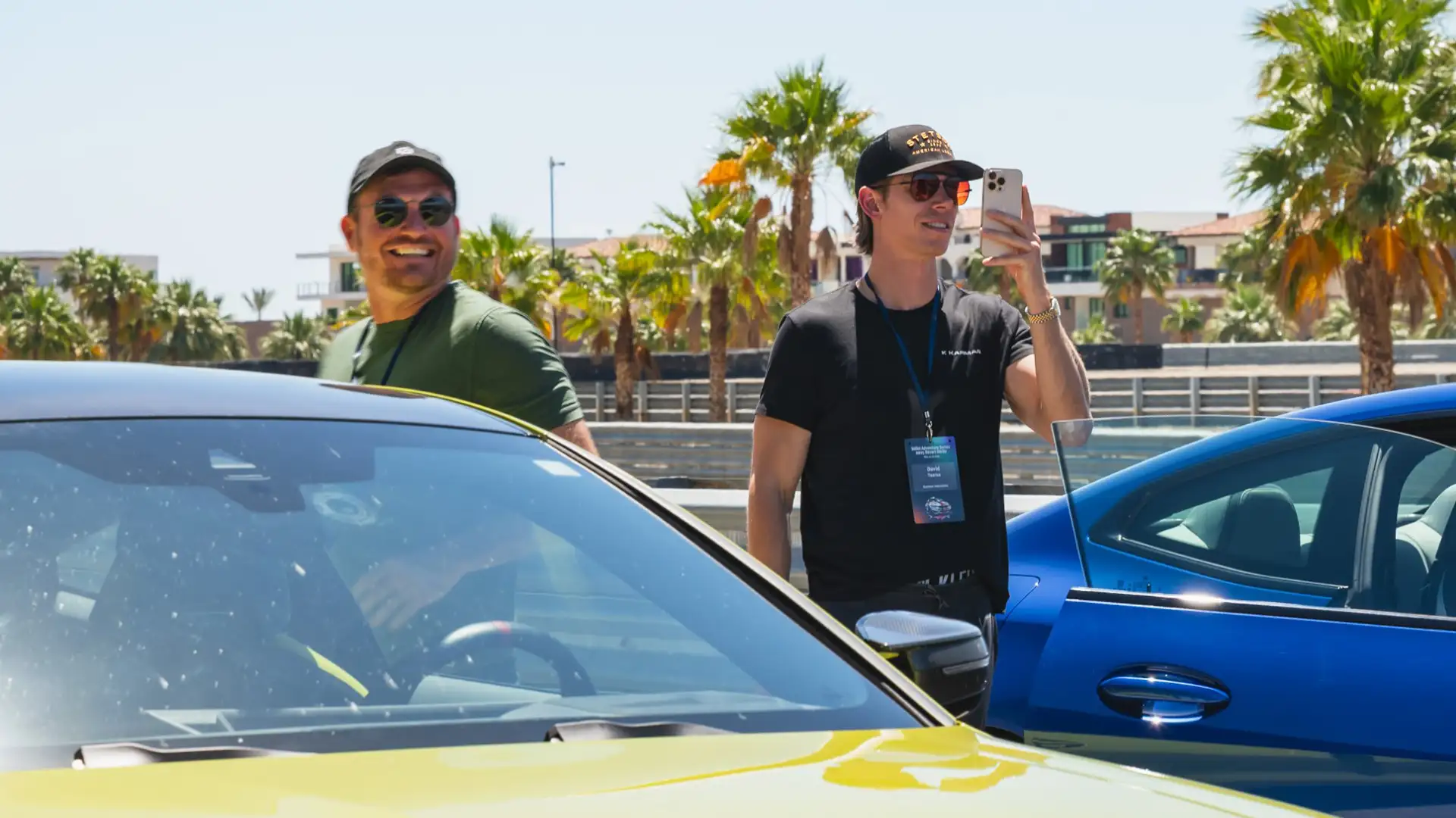 Two guests beside the cars, one taking a photo on his phone