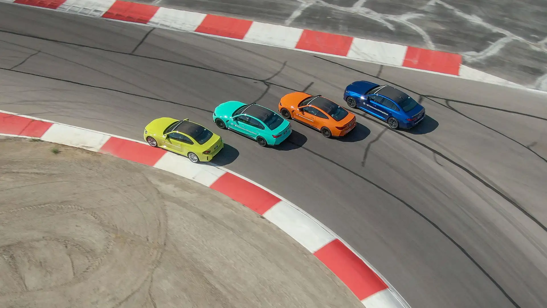 Four BMW M cars nose to tail through a red-and-white kerbed corner, seen from above