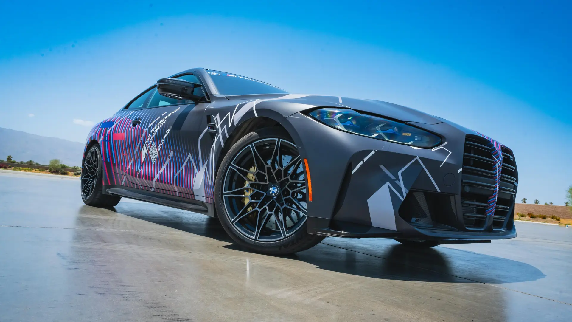 The mixed-reality BMW M4 in its graphic wrap parked on the apron
