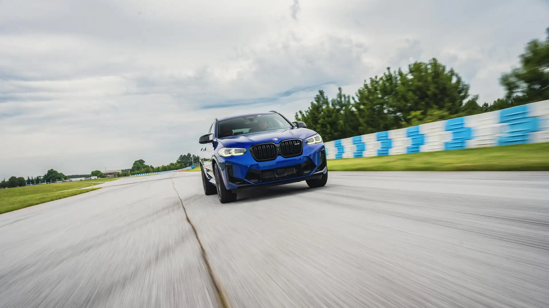 Blue BMW X3 M at speed on the circuit past the barriers