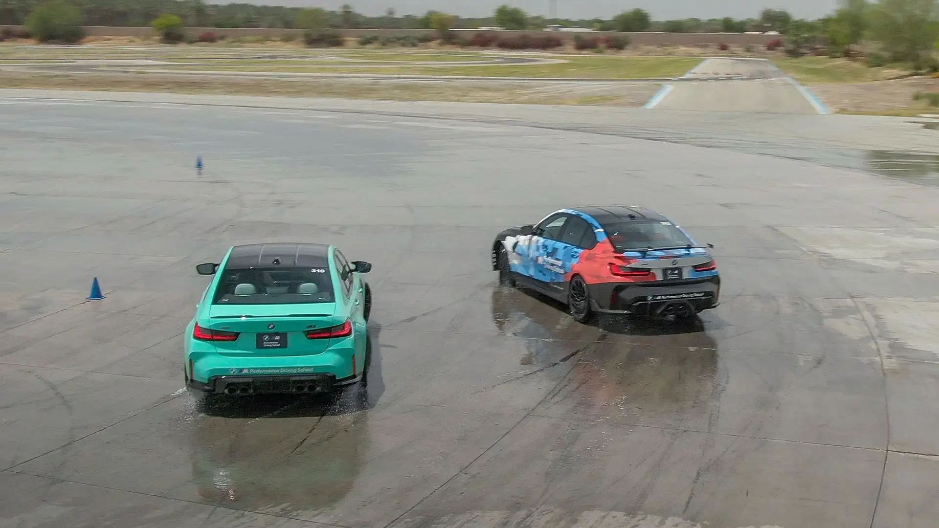 Mint green BMW M3 and a liveried M2 side by side on the wet pad, seen from above