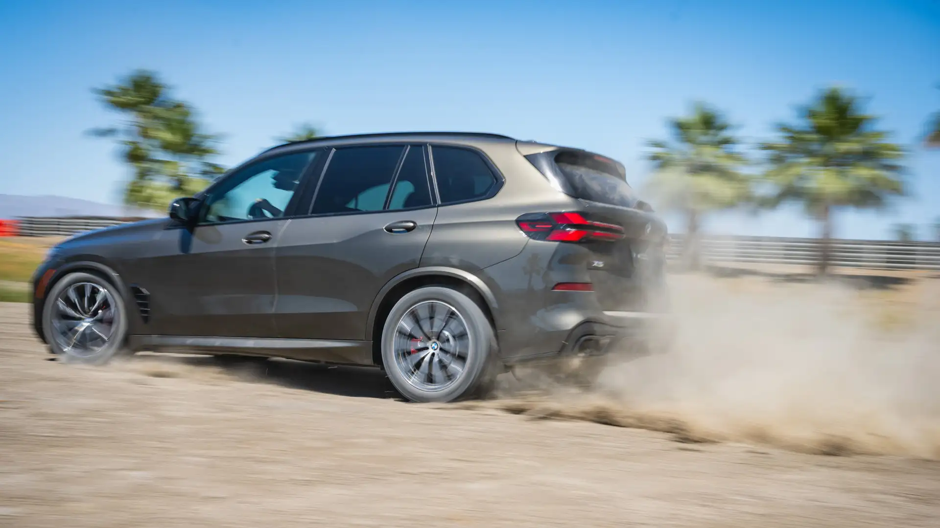 Dark BMW X5 kicking up dust along the gravel course