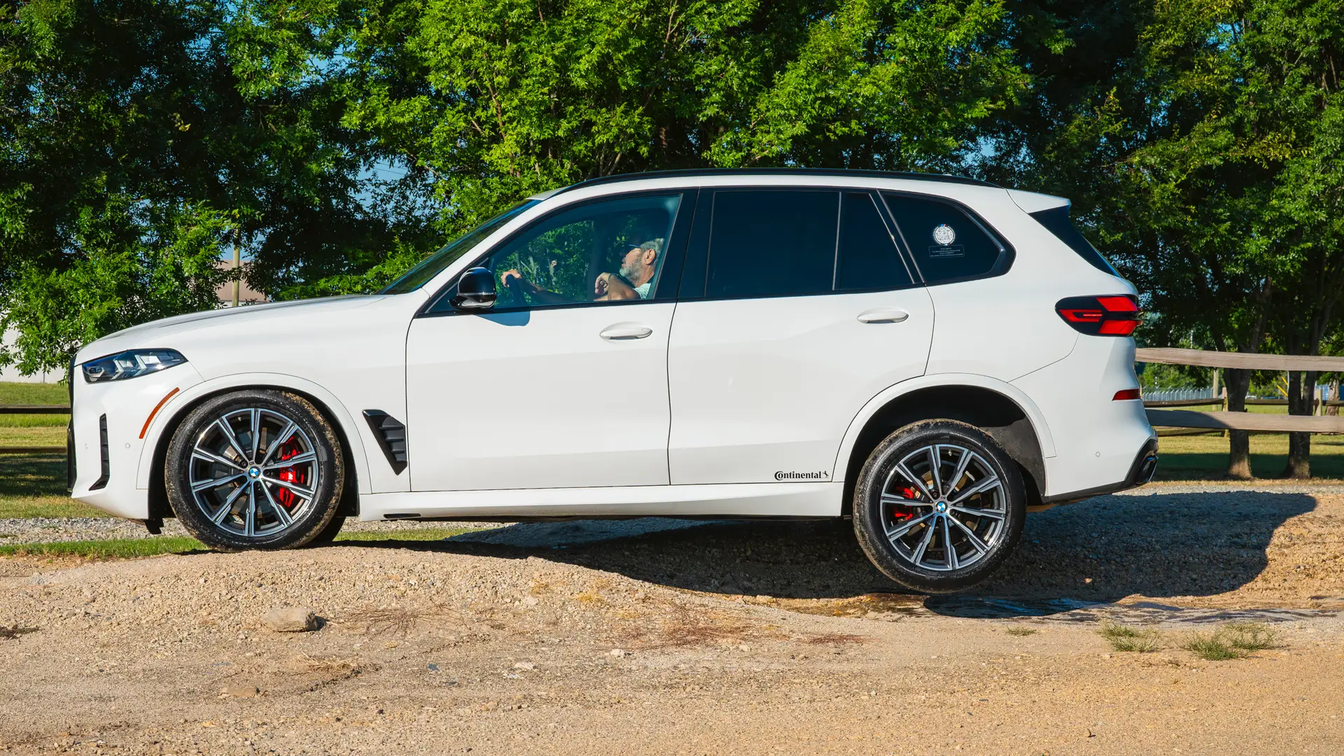 White BMW X5 parked on a gravel trail beside trees