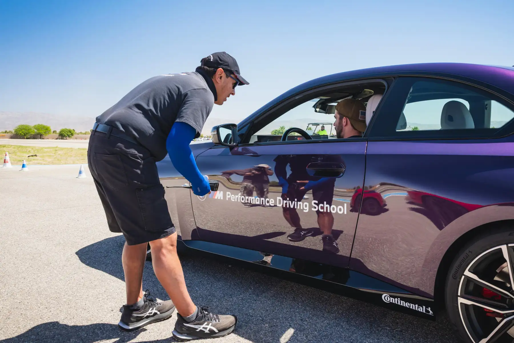 Instructor crouching at the window of a purple BMW M2 to brief the driver