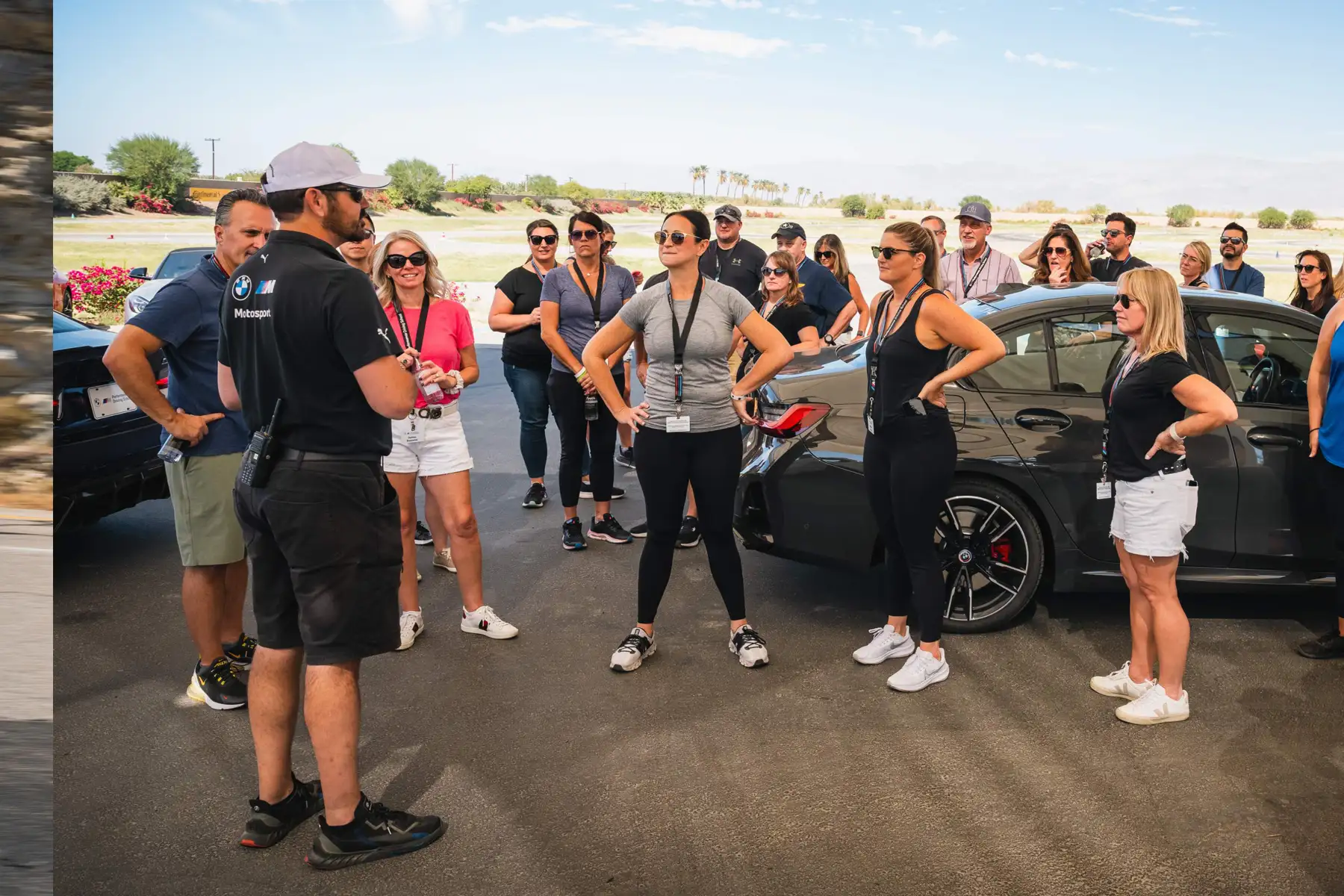 Instructor briefing a large group of guests beside the cars in the desert paddock