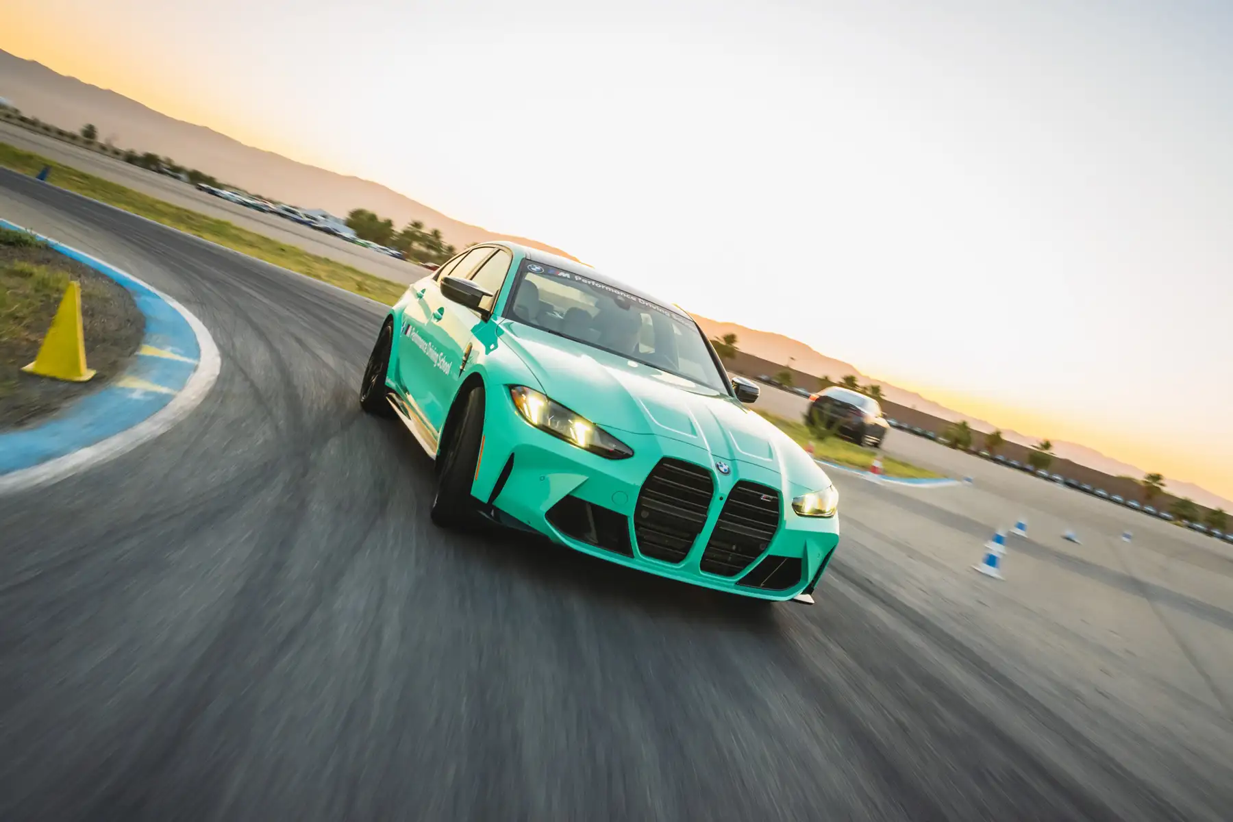 Mint green BMW M3 cornering on the desert circuit at dusk