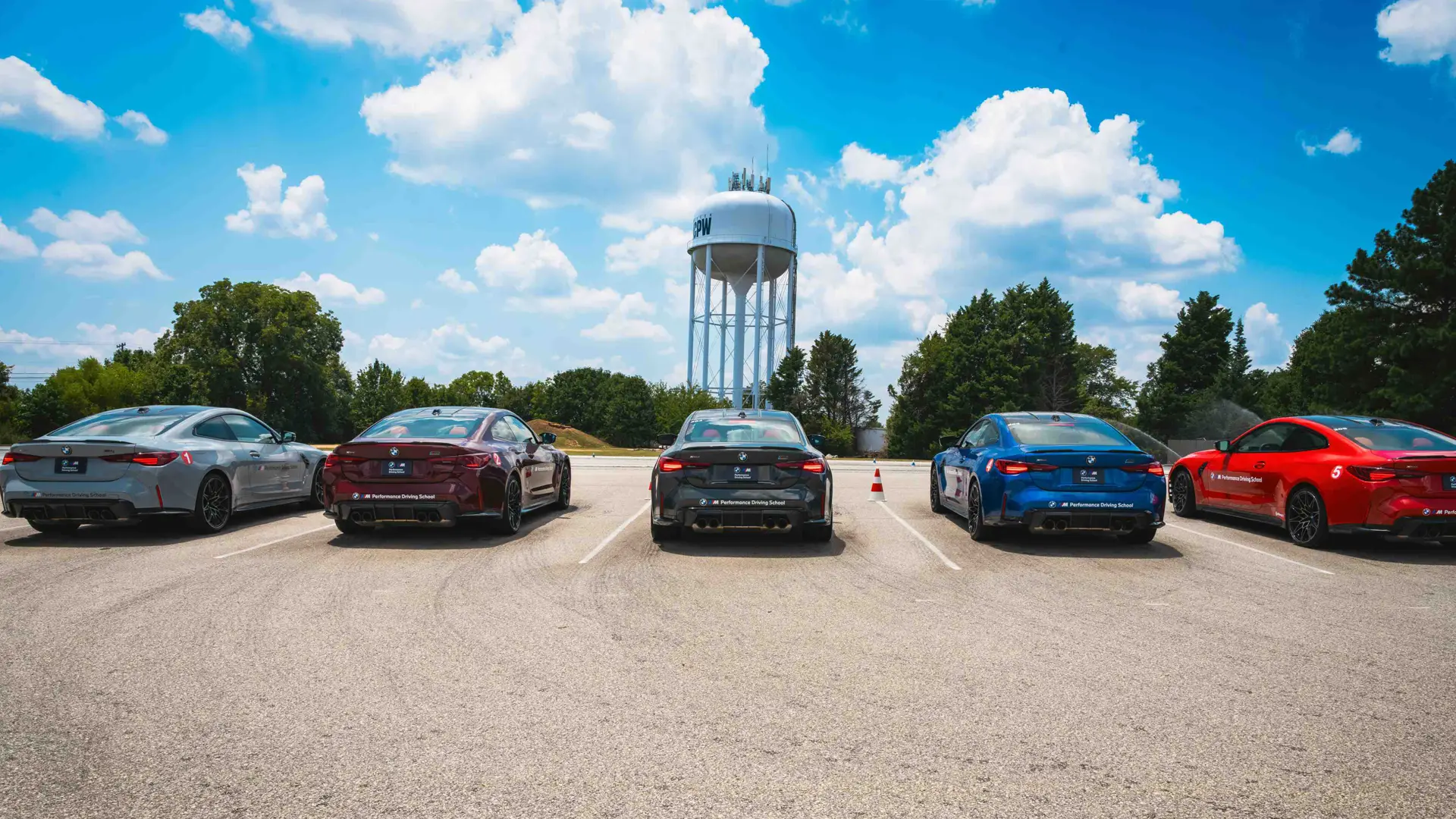 Five BMW M4s parked in a row beneath the water tower