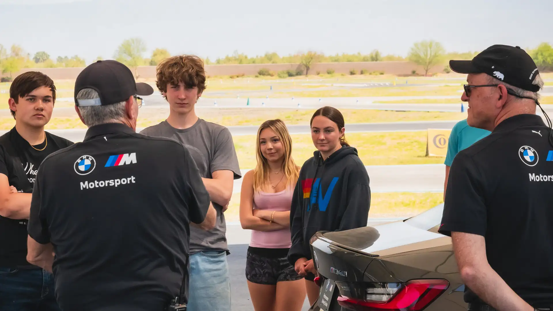 Two instructors briefing a group of teenagers beside a BMW