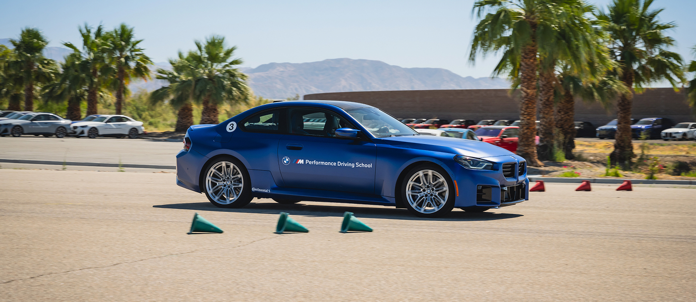 Blue BMW M2 running a coned course with palms and mountains behind
