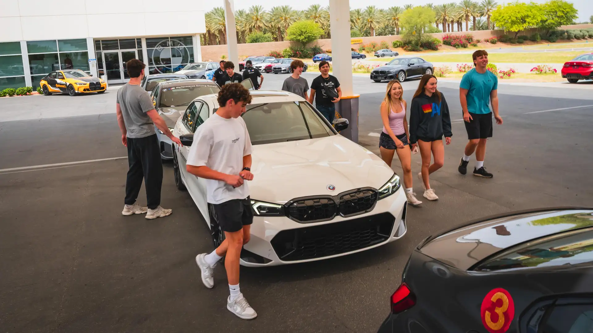 Teenage students gathering around a white BMW M340i outside the Performance Center