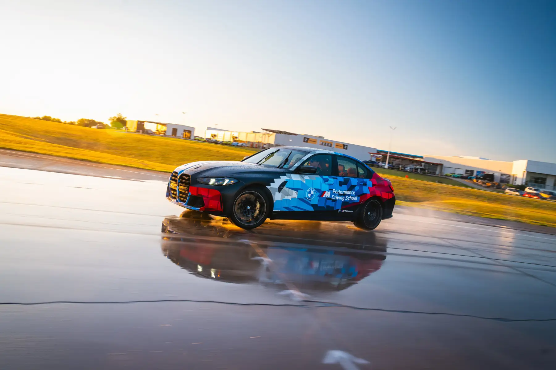 BMW M3 in Motorsport livery sliding across the wet pad at sunset
