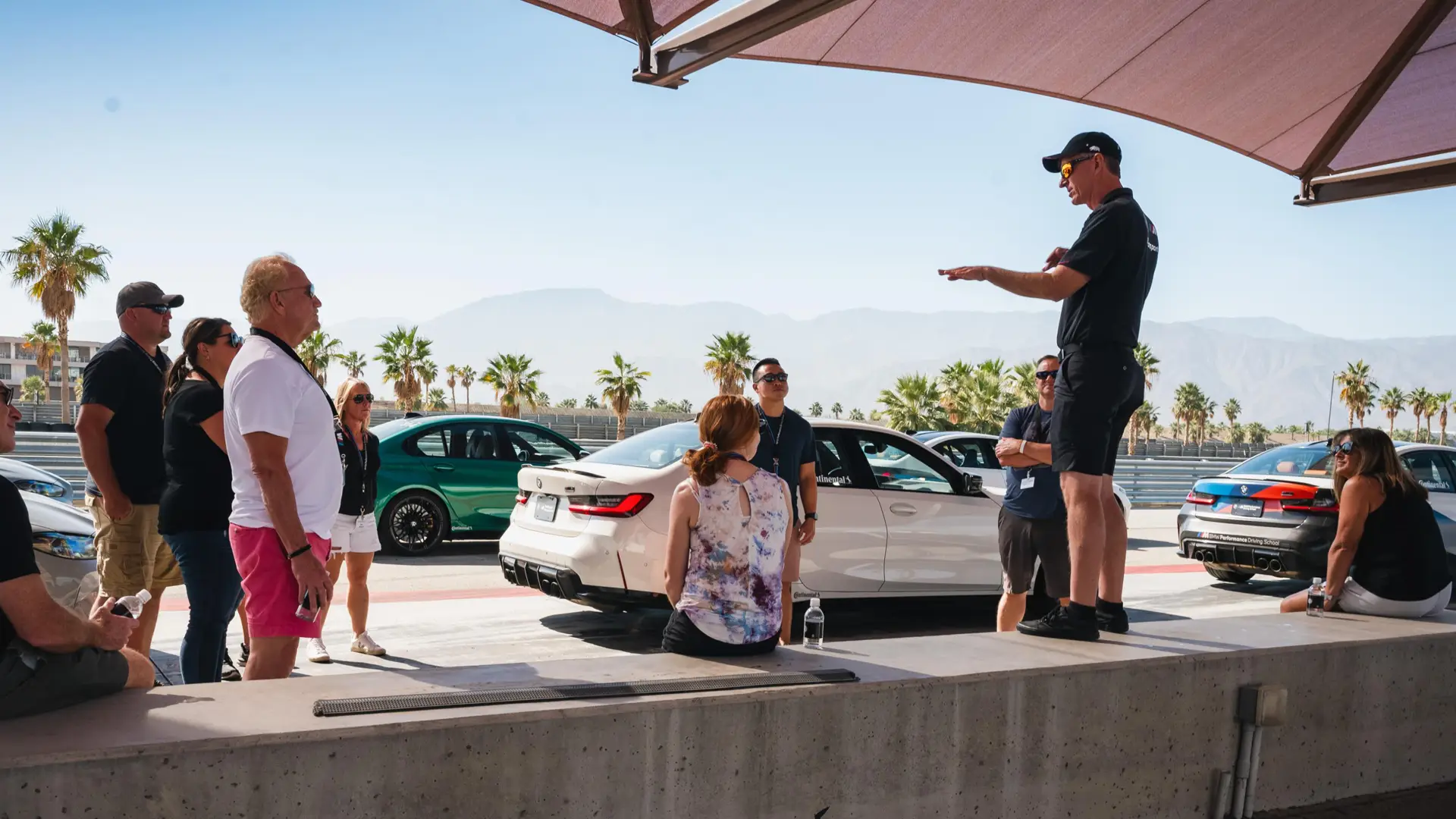 Instructor briefing a group seated under the canopy beside the M cars