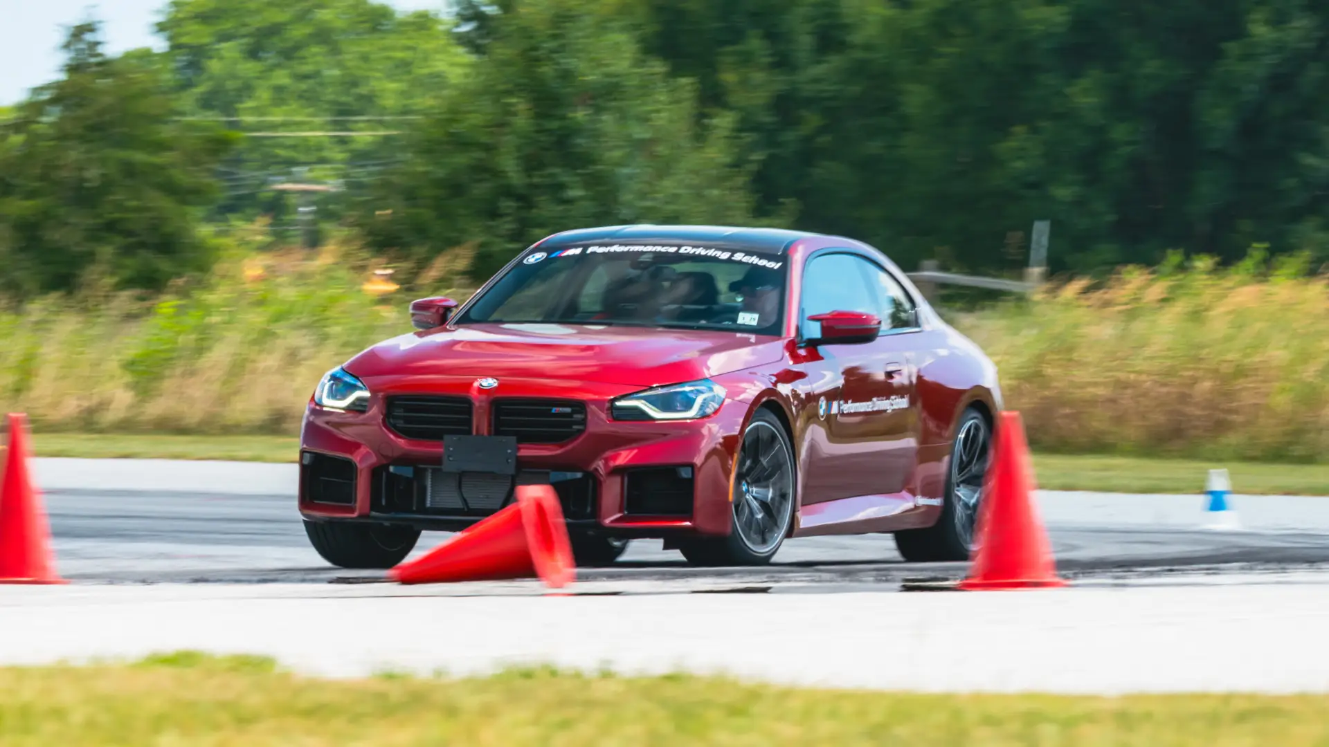 Red BMW M2 cornering past a line of orange cones