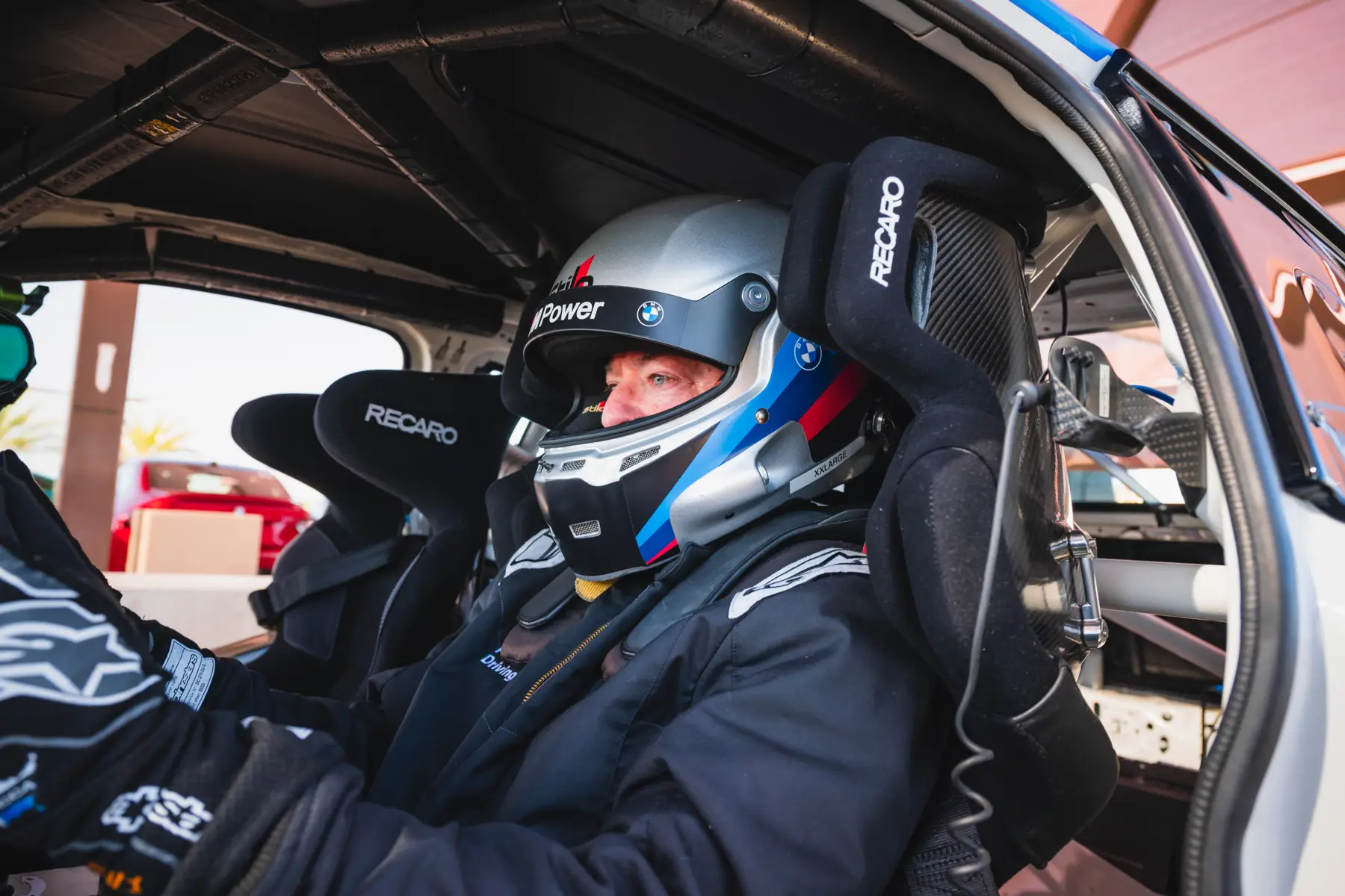 Driver in a helmet and race suit strapped into a caged BMW race car