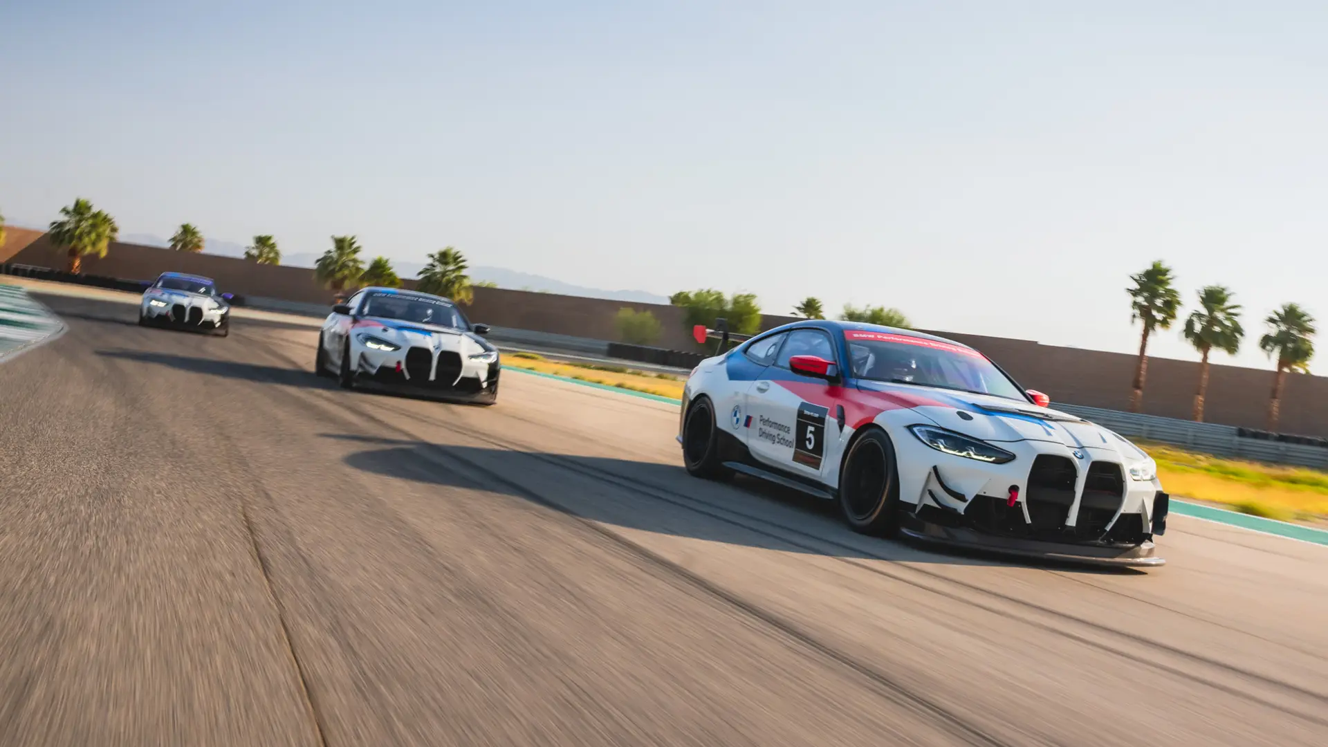 Three BMW M4 GT4 race cars running nose to tail on the circuit