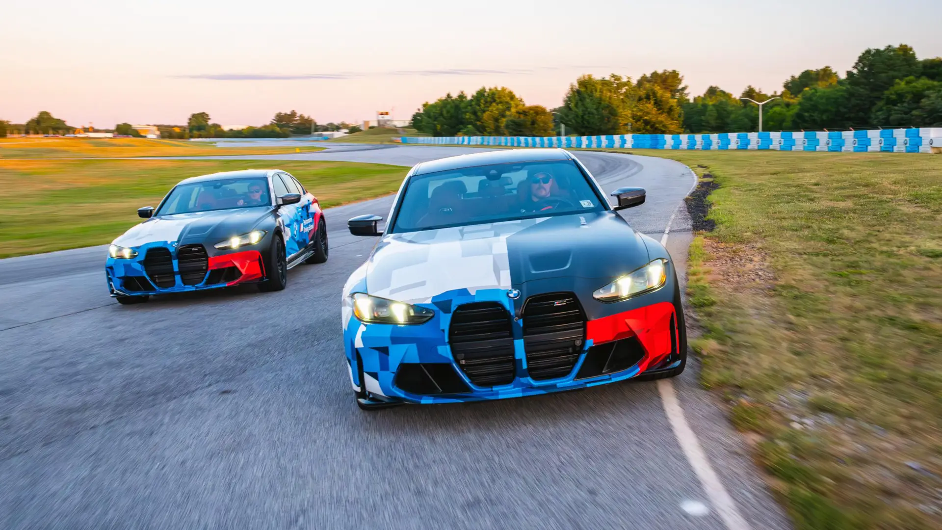 Two BMW M4s in Motorsport livery running nose to tail on the circuit at dusk