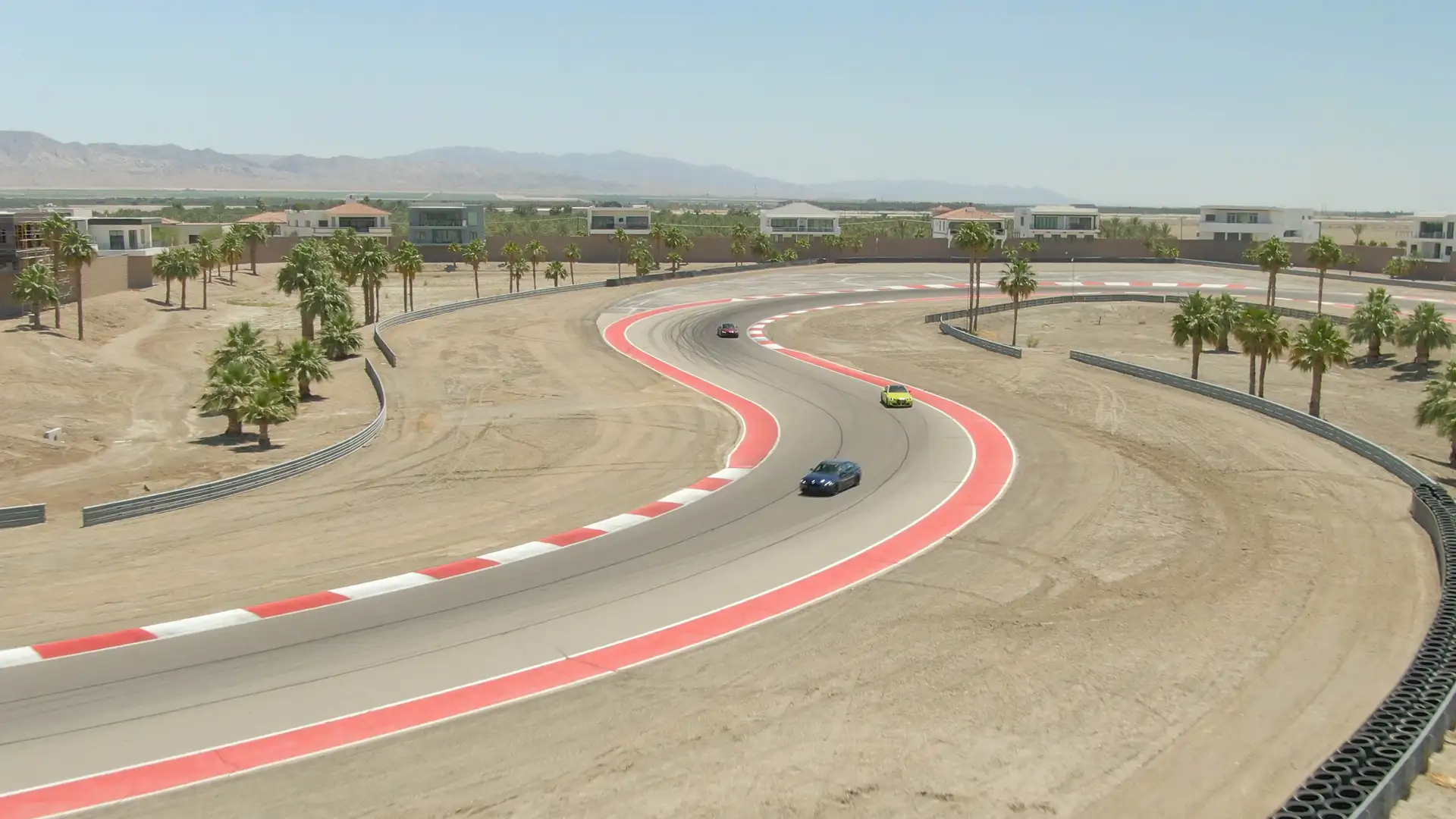 Cars running the red-and-white kerbed corners of the desert circuit at The Thermal Club