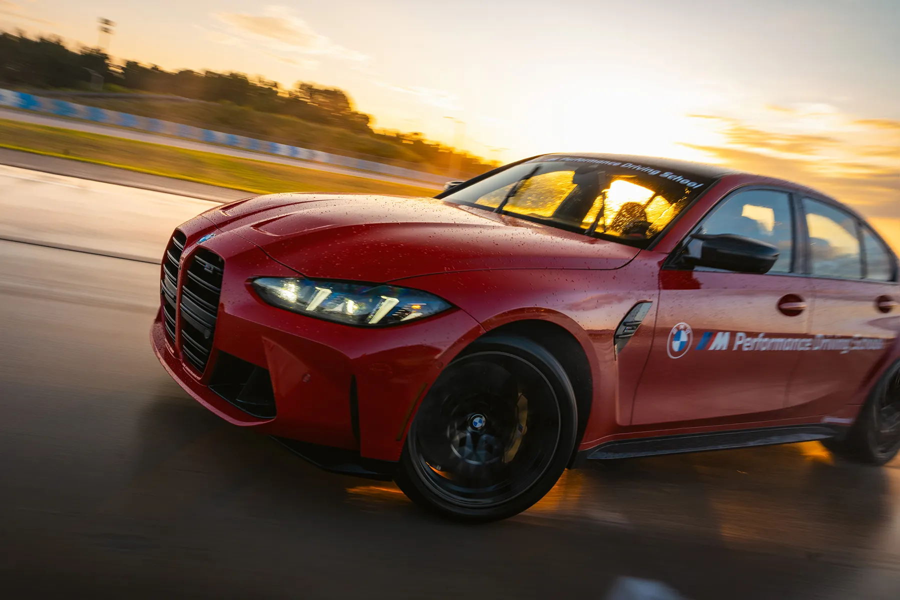 Red BMW M3 at speed on the wet circuit at sunset