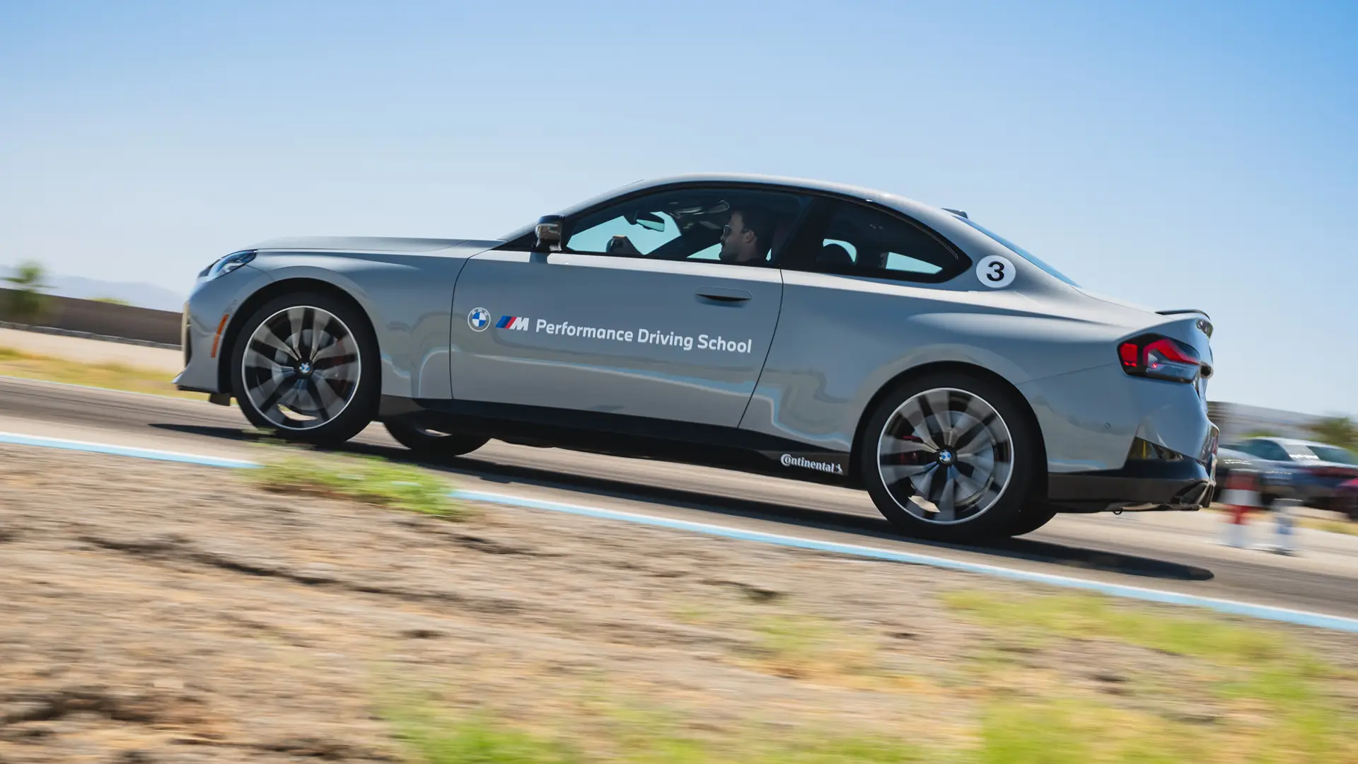 Grey BMW M2 at speed alongside the blue-edged circuit