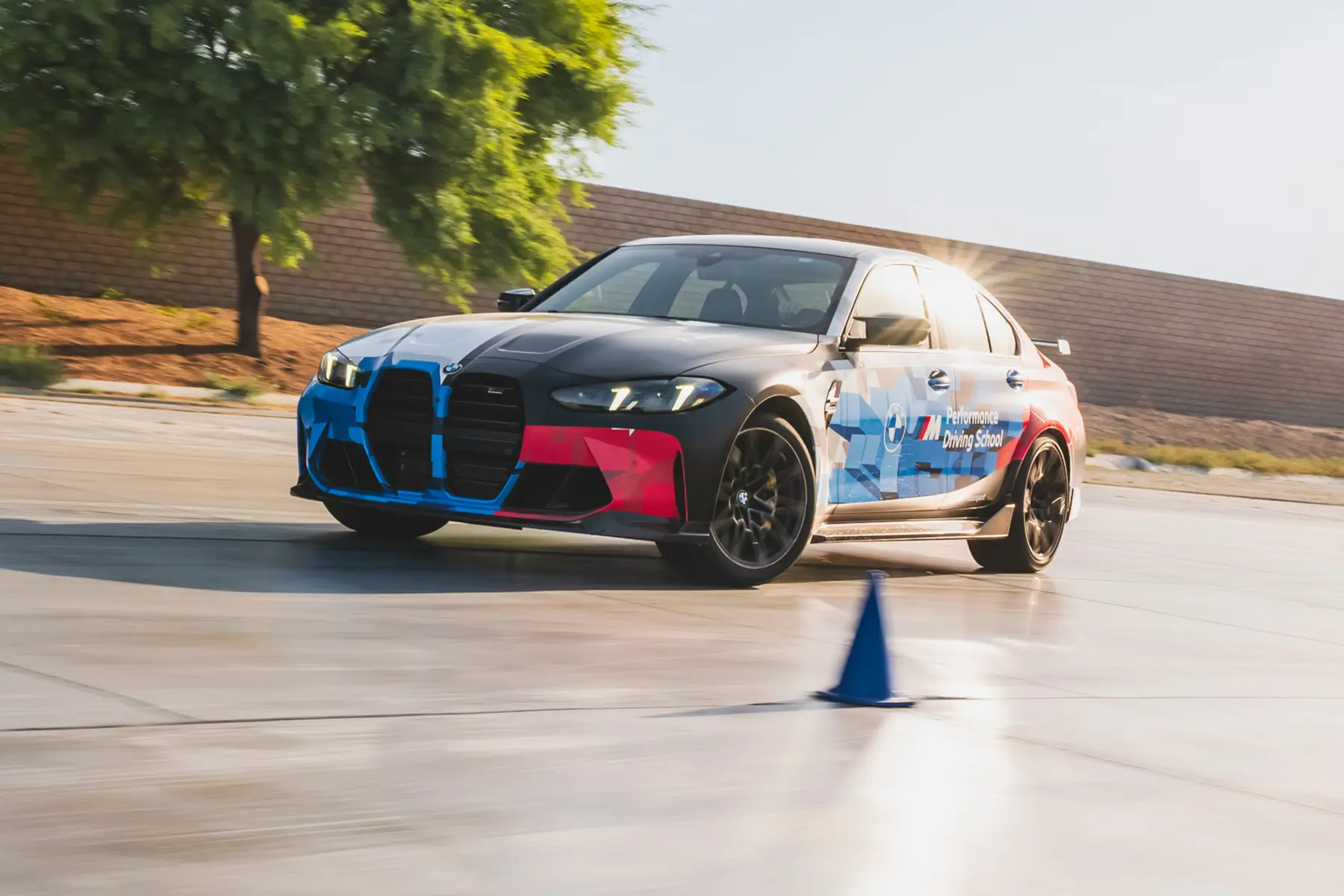 BMW M3 in Motorsport livery sliding past a blue cone on the wet pad