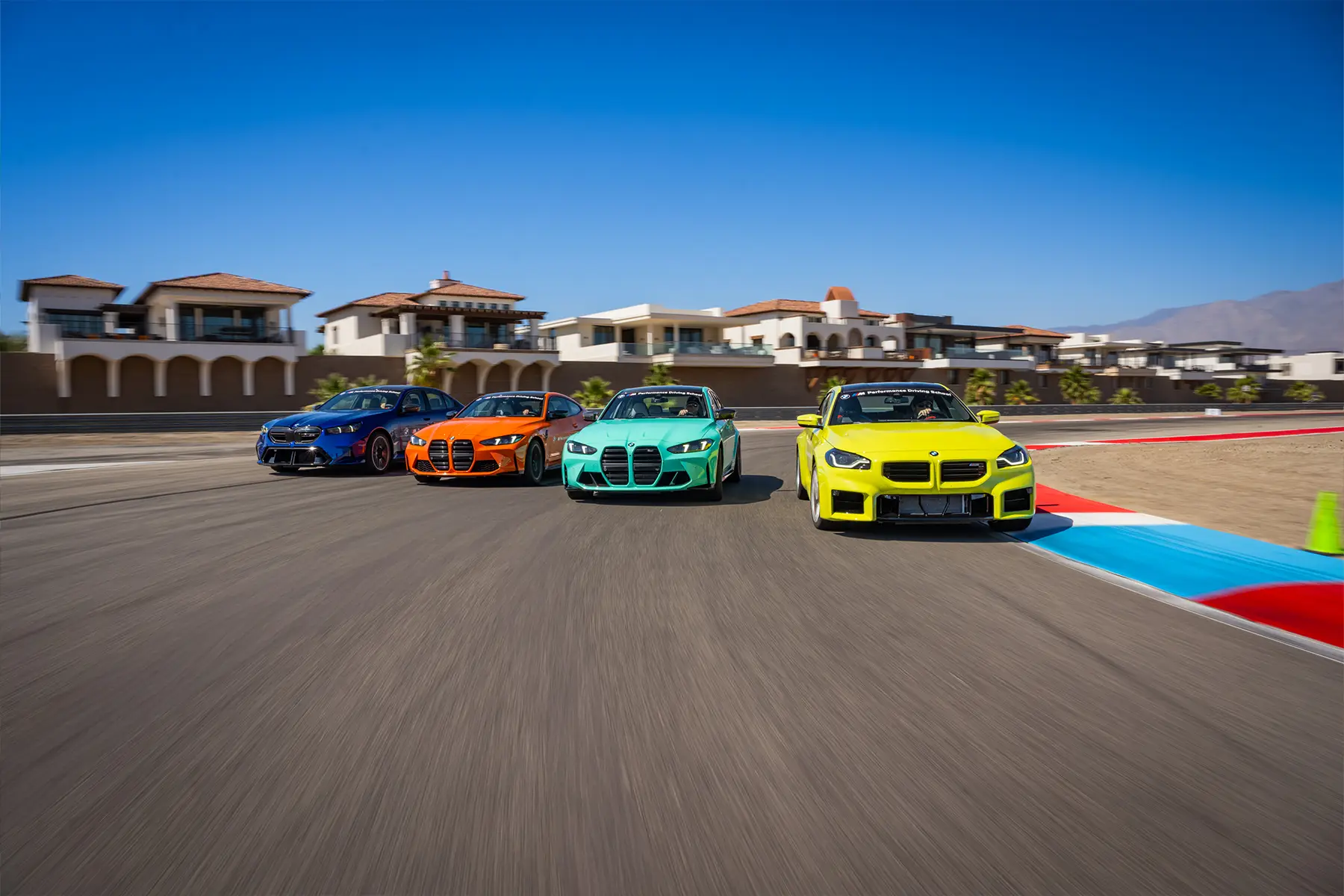 Four BMW M cars running abreast on the desert circuit, led by a yellow M2