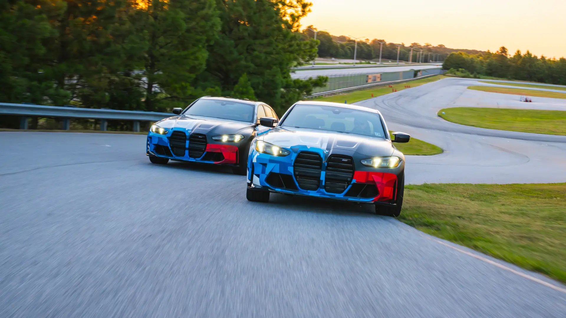 Two BMW M3s in Motorsport livery running side by side at sunset