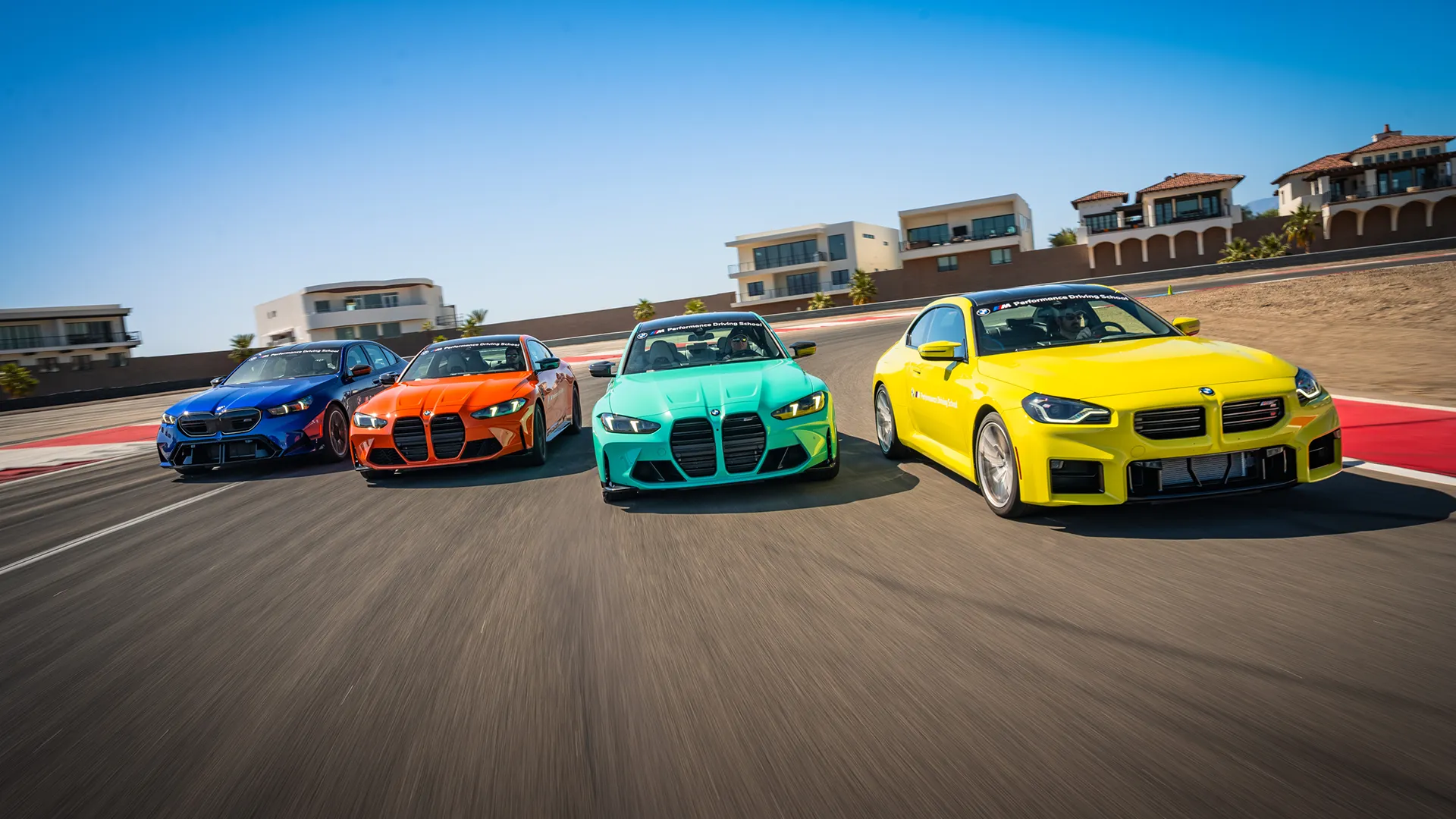 Four BMW M cars running abreast on the desert circuit, led by a yellow M2
