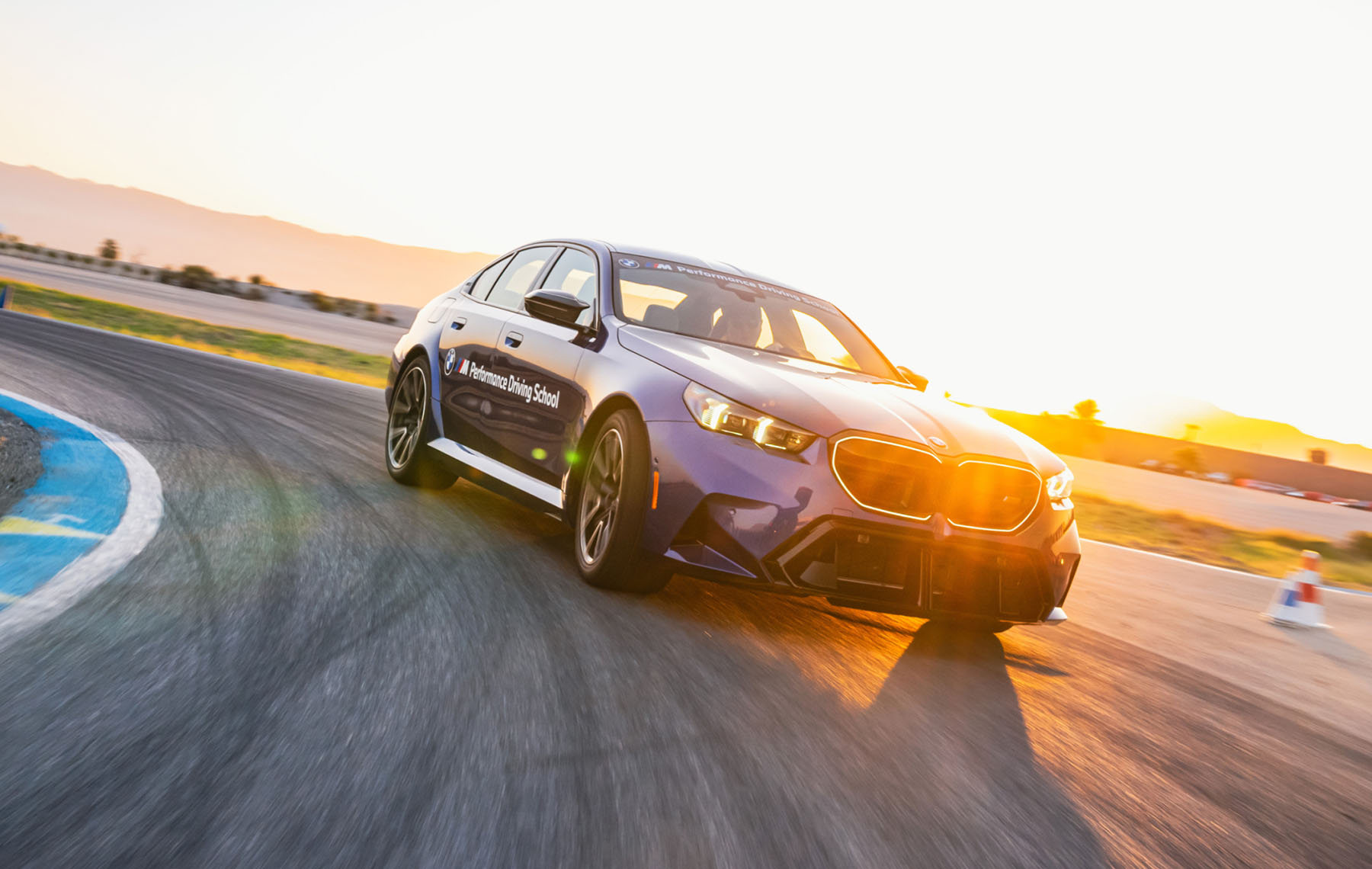 Purple BMW M5 cornering into a low sun on the desert circuit