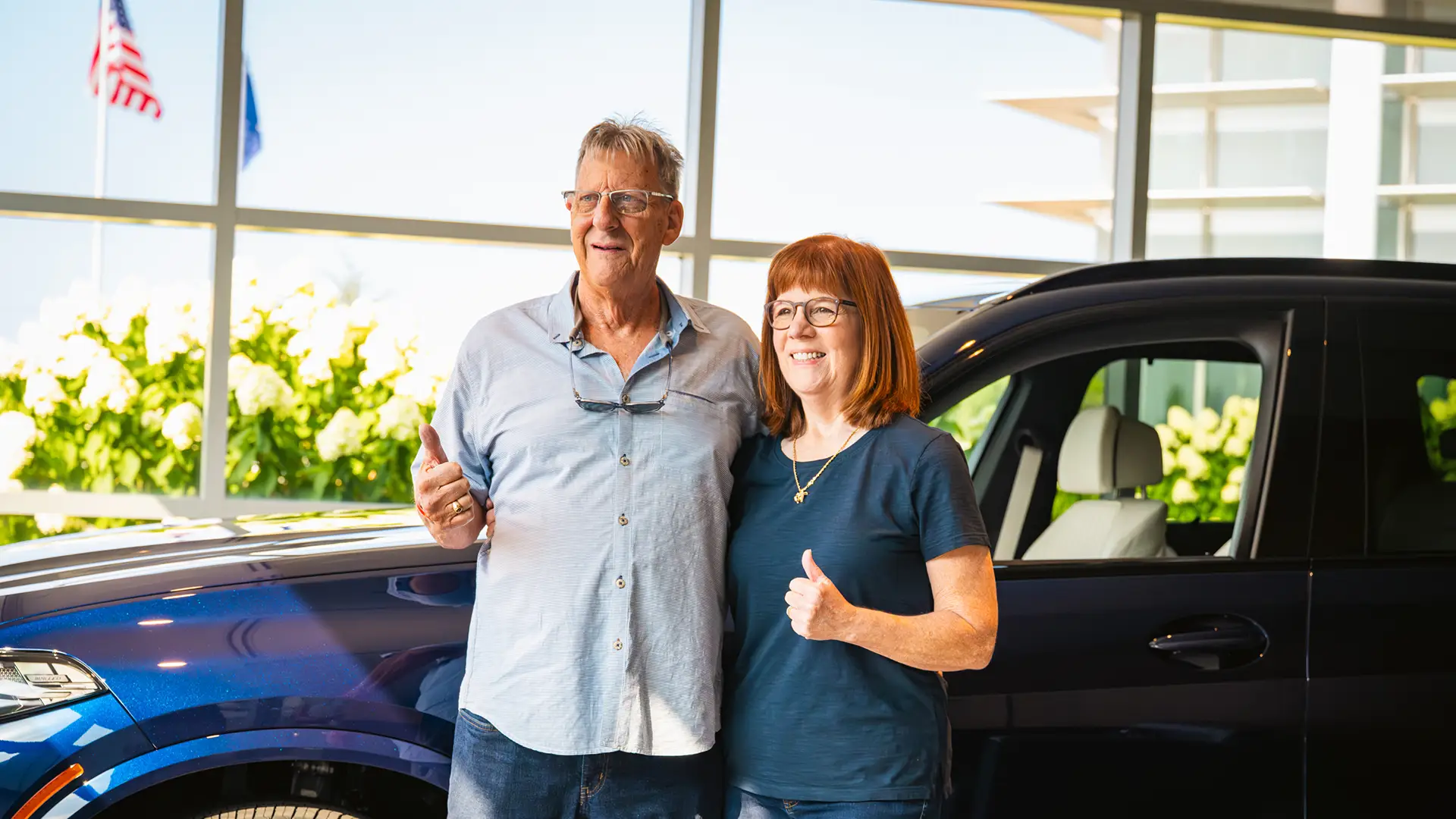 Couple giving a thumbs up beside their new BMW at the delivery centre