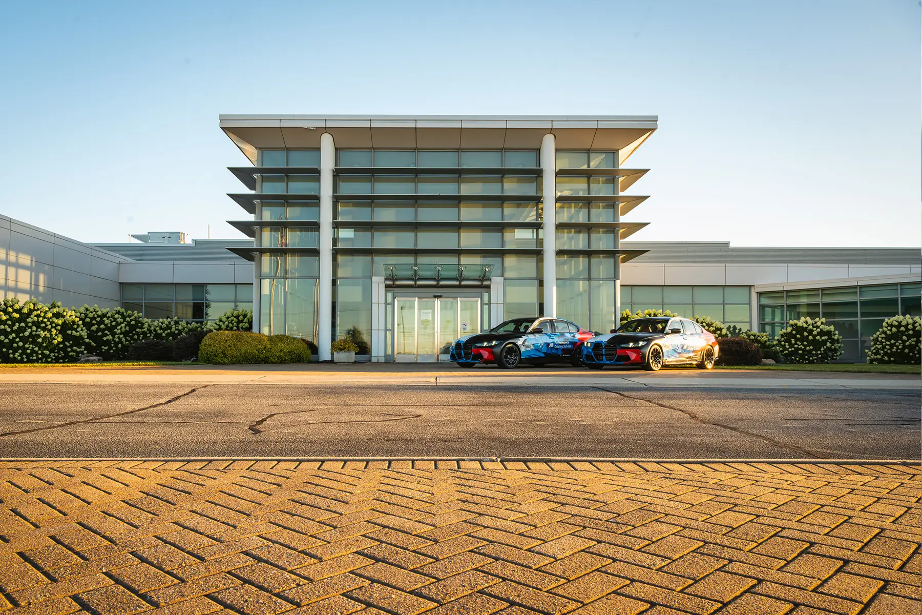 Two BMW M cars in Motorsport livery parked outside the Performance Center entrance
