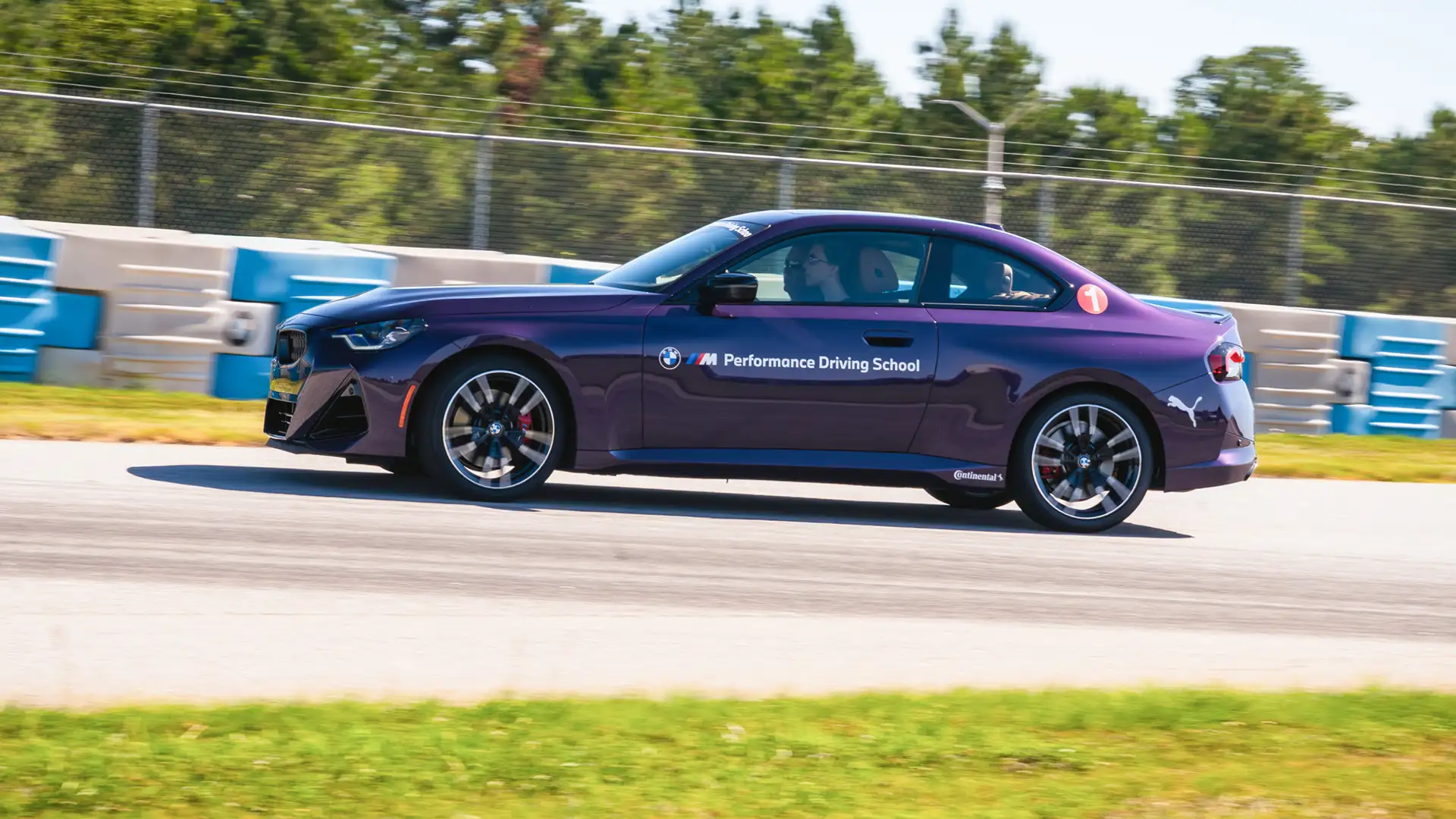 Purple BMW M2 at speed on the circuit past the barriers