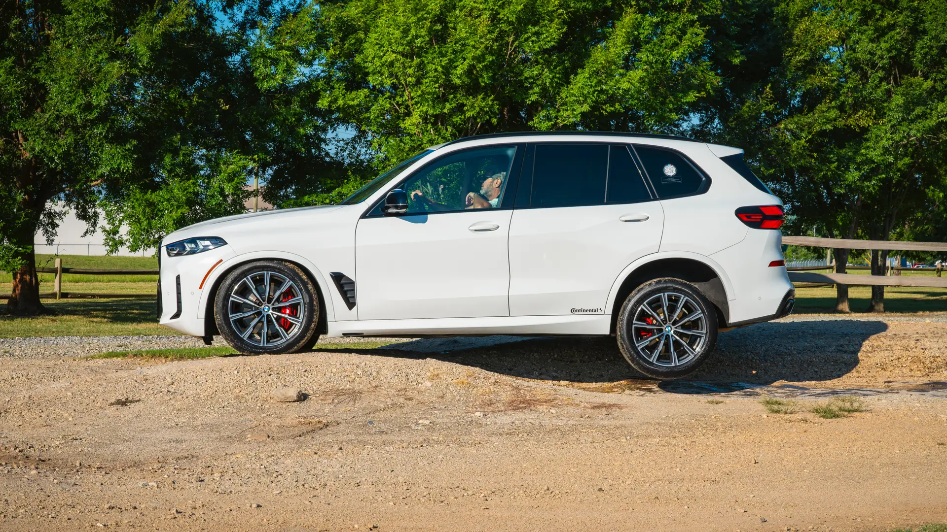 White BMW X5 parked on a gravel trail beside trees
